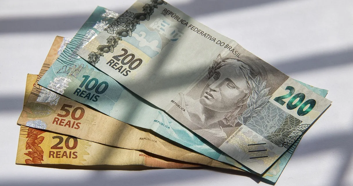 Notas de real de 20, 50, 100 e 200 espalhadas sobre uma superfície branca